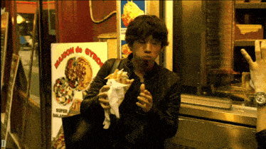 a man eating a sandwich in front of a sign that says maison de gyros on it