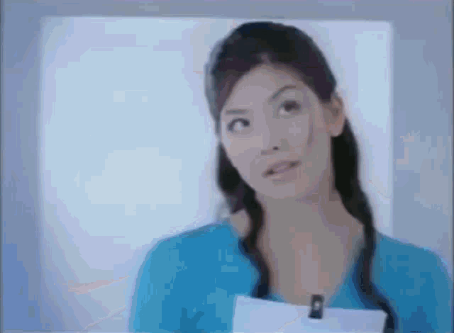 a woman in a blue shirt is holding a piece of paper and looking up at something .