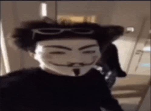 a man wearing a anonymous mask and glasses is standing in a hallway .