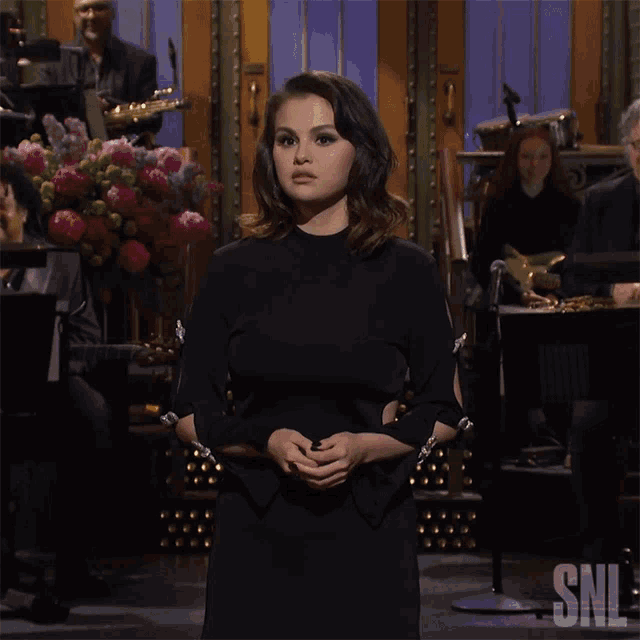 a woman in a black dress is standing in front of a snl logo