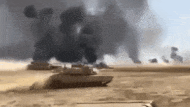 a group of tanks driving through a desert with smoke coming out of them .