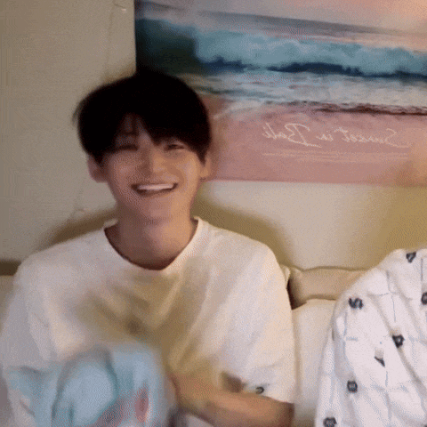 a young man is smiling while sitting on a bed in front of a poster of the ocean .