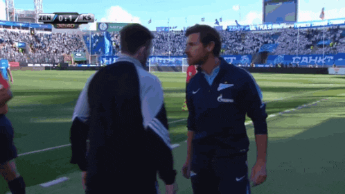 two men shake hands on a soccer field with a scoreboard that says zen 0:17