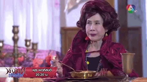 a woman in a red dress is sitting at a table with a spoon in her mouth .