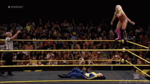 a woman is doing a handstand in a wrestling ring while a referee watches .