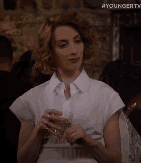 a woman in a white shirt is holding a glass of water in her hand