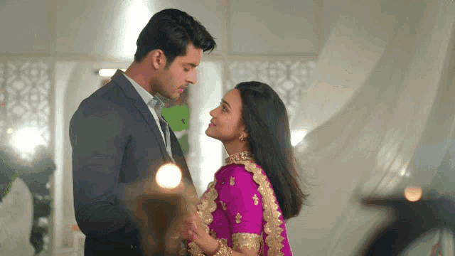 a man in a suit and a woman in a pink dress are looking into each other 's eyes