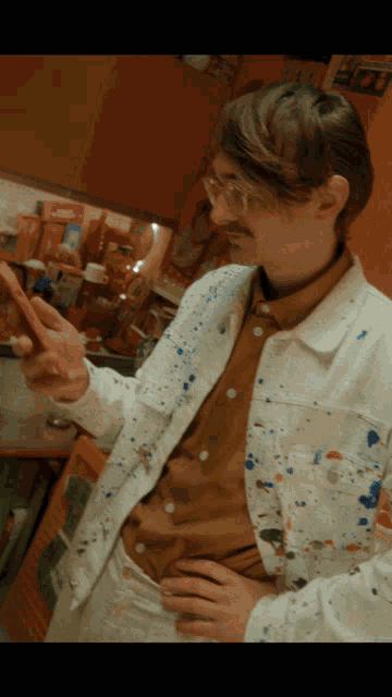 a man wearing a white jacket with blue spots on it holds a cell phone