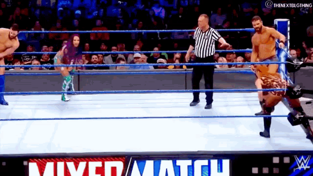 a referee is standing in the middle of a wrestling ring while two wrestlers are in the ring .