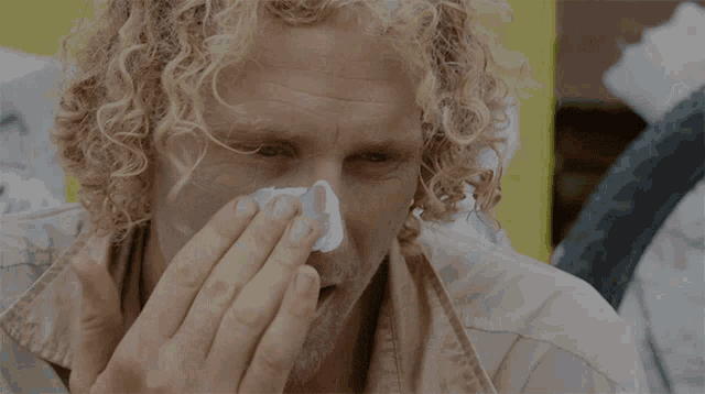 a man with curly hair is holding a bandage to his nose