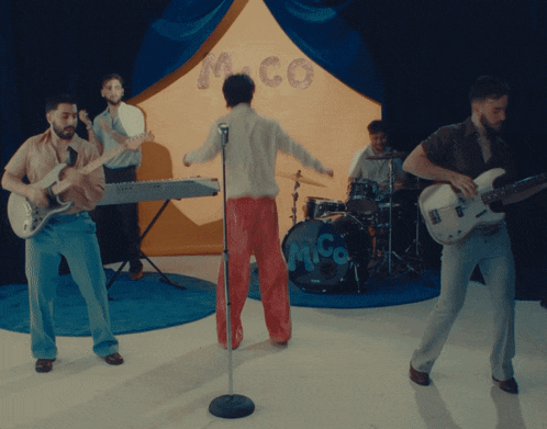 a man singing into a microphone in front of a drum set that says m-co