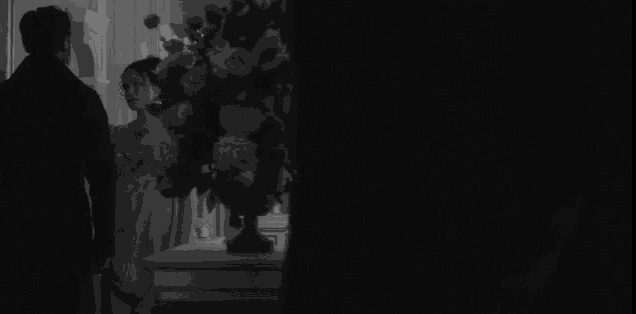a man and woman are standing in front of a vase of flowers .