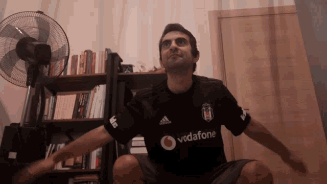 a man wearing a black vodafone shirt is squatting with his arms outstretched