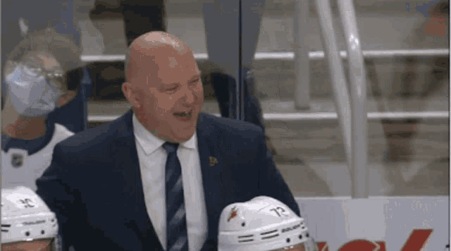 a man in a suit and tie is laughing in front of a hockey player wearing a mask