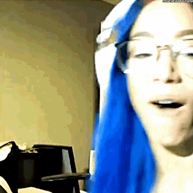 a woman with blue hair is wearing glasses
