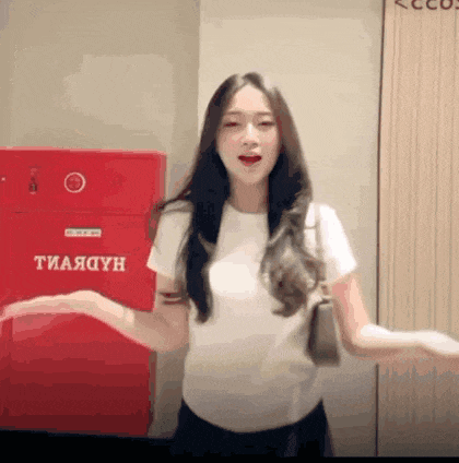 a woman in a white shirt is standing in front of a red box that says тиаядун