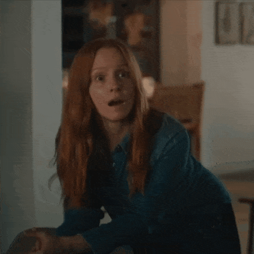 a woman with red hair and a surprised look on her face is wearing a blue shirt
