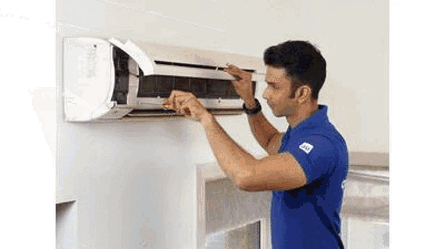a man in a blue shirt is cleaning an air conditioner on a wall .