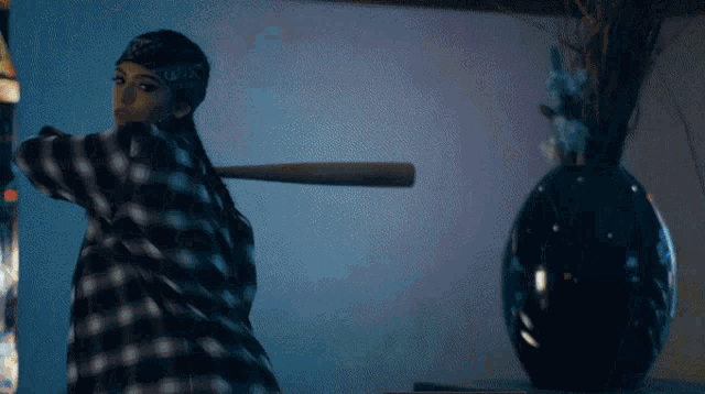 a woman in a plaid shirt is holding a baseball bat in front of a black vase