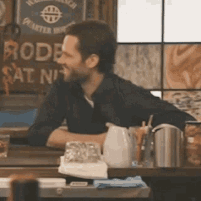 a man sits at a bar in front of a sign that says rodeo at night