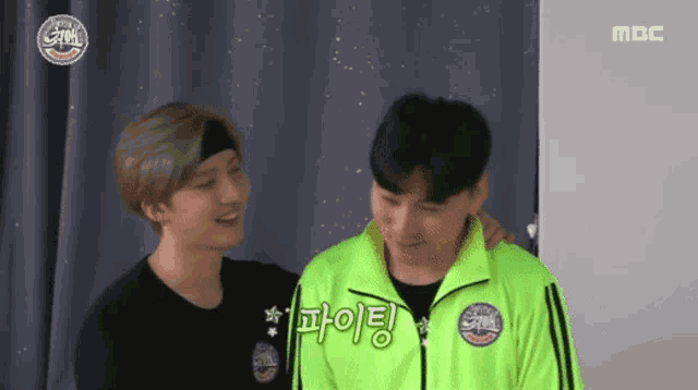 two men are standing next to each other and one of them is wearing a green jacket that says mbc