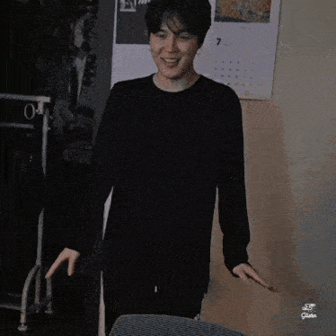 a young man in a black shirt is standing in a room with his arms outstretched and smiling .