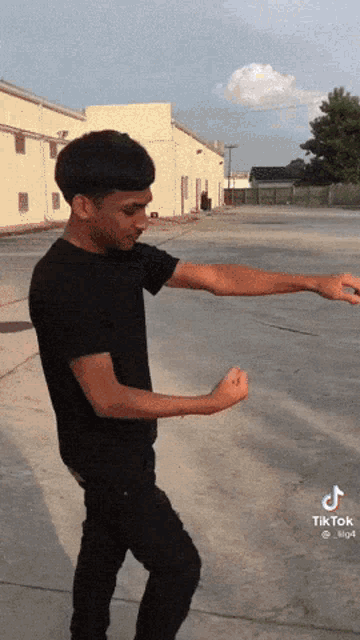 a man in a black shirt is standing in a parking lot with his arms outstretched and a tiktok logo on the bottom left