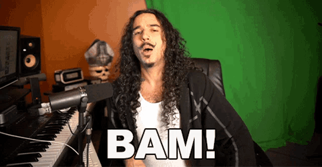 a man with long curly hair is singing into a microphone and the word bam is on the bottom