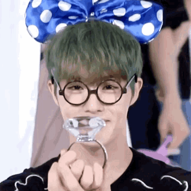 a man with green hair wearing glasses and a blue bow on his head holds a diamond in his hand .
