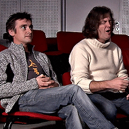 two men are sitting in red chairs with one wearing a sweater that says ' abercrombie ' on it