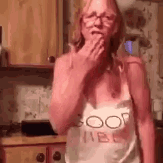 a woman wearing glasses and a tank top is covering her mouth in a kitchen .