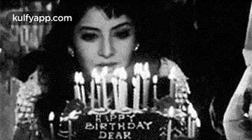 a black and white photo of a woman blowing out candles on a cake .