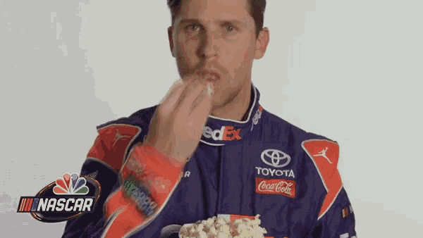 a man in a racing suit is eating popcorn from a cup .