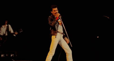 a man in a leather jacket is singing into a microphone while another man plays a guitar on stage .
