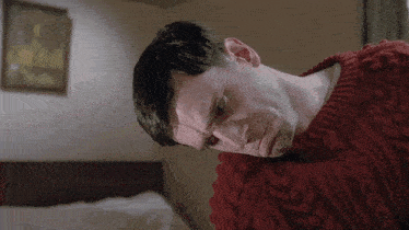 a man in a red sweater is laying on a bed looking down