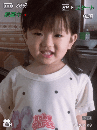 a little girl wearing a white shirt that says baby three on it
