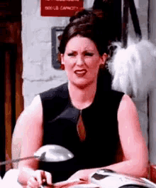 a woman in a black tank top is sitting in front of a lamp holding a magazine .