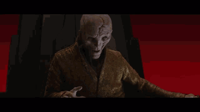 a man in a gold robe is sitting in a dark room with a red background .