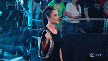 a woman is holding a championship belt in front of a crowd and a sign that says live