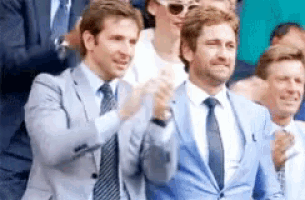 a group of men in suits and ties are clapping in a crowd .