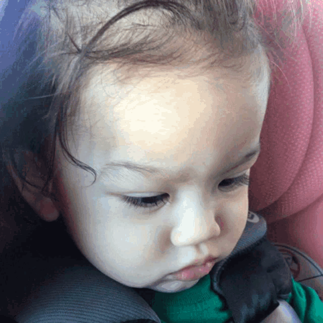 a baby is sitting in a car seat with a pink shirt on