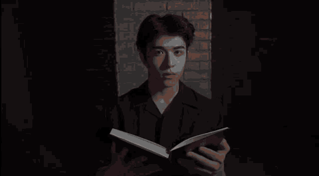 a young man is reading a book in front of a brick wall