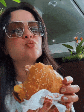 a woman wearing sunglasses is eating a hamburger with a burger king logo on it