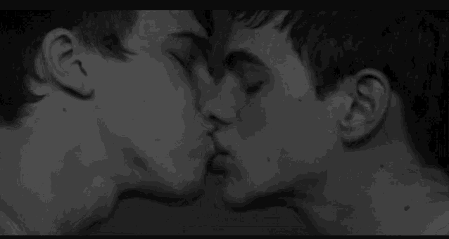 two men are kissing in a black and white photo .