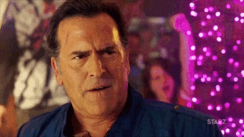 a man in a blue shirt is standing in front of a crowd of people in a club .