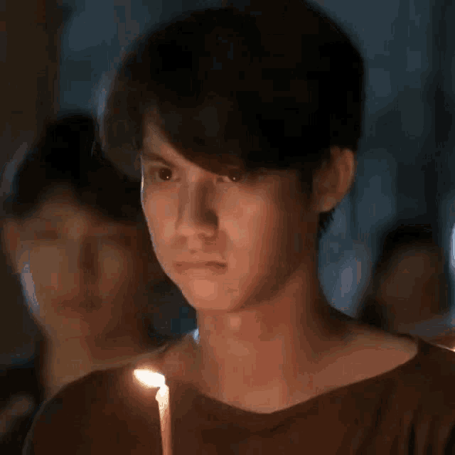 a young man is holding a lit candle in front of his face .