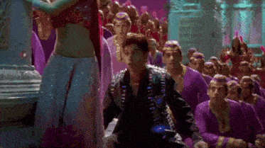 a man is sitting in front of a crowd of people in purple clothes .