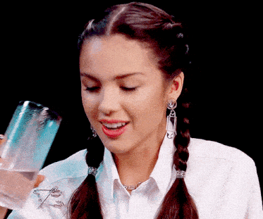 a woman with pigtails and safety pins in her earrings is holding a glass of water