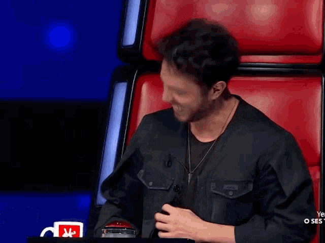 a man in a black jacket is sitting in a red chair and smiling