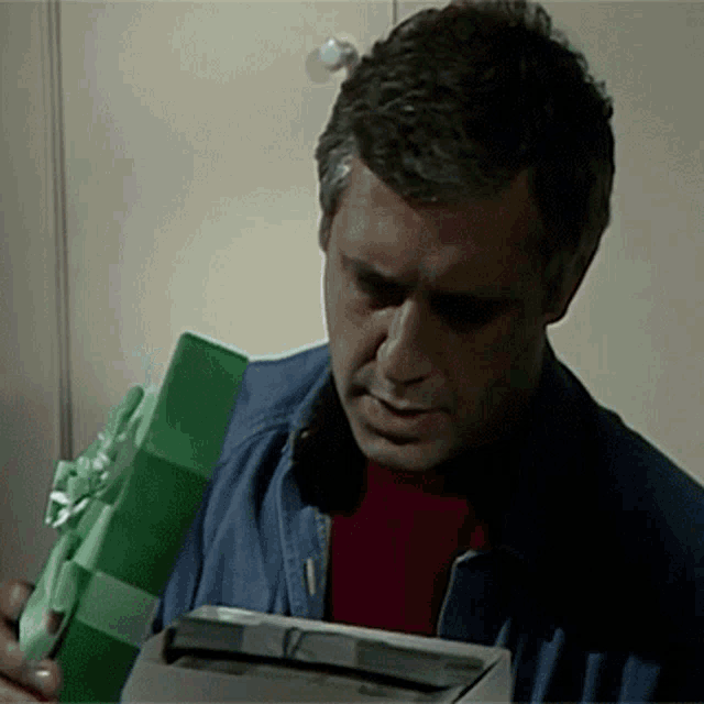 a man in a blue jacket is holding a green and white gift box
